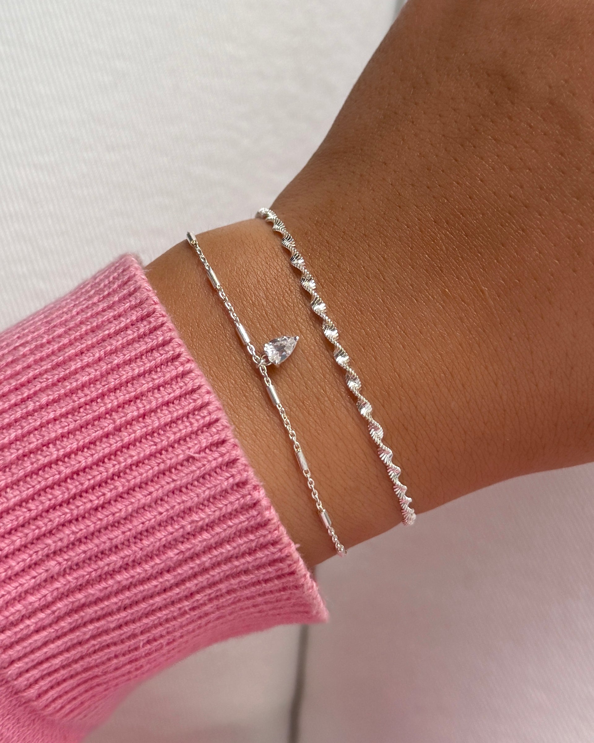 A close-up of a model's wrist, showing the Katie Bracelet Silver with its delicate charm layered with the sparkling Herringbone Twisted Bracelet in silver.