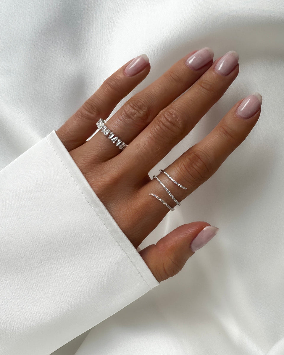 A model's hand wearing the Sparkle Wrap Ring in silver on the ring finger and the Iggy Ring in silver on the index finger, both adorned with sparkling cubic zirconia stones.