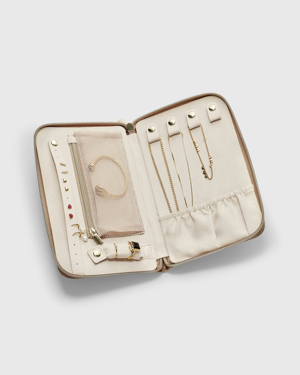 The Jewelry Travel Case in beige, shown open and filled with an assortment of gold jewelry, including necklaces, rings, a bracelet, and multiple pairs of earrings, showcasing its organizational features.