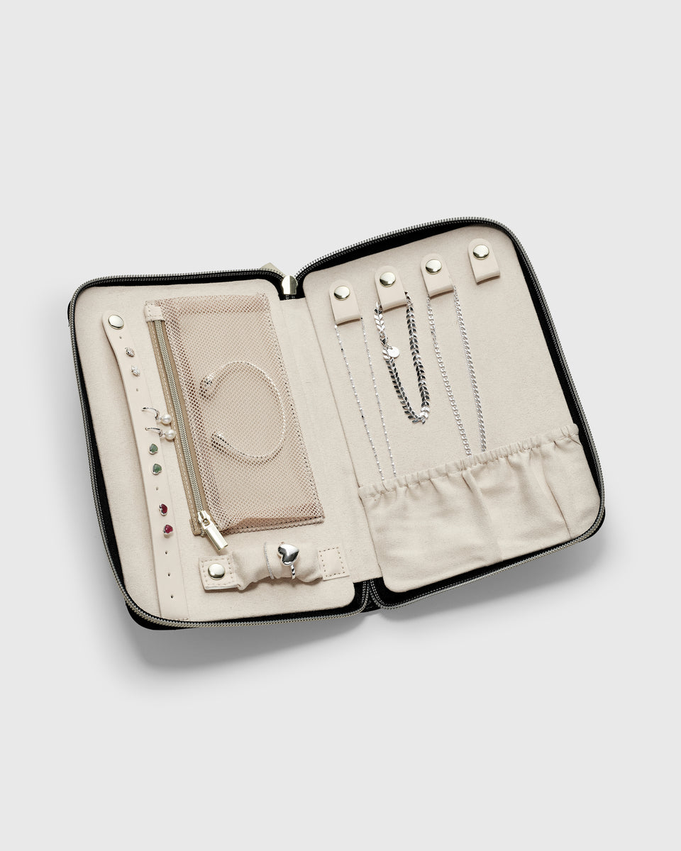 An open black Jewelry Travel Case with a beige interior, showcasing how it neatly organizes various silver pieces, including necklaces, a bracelet, stud and drop earrings, and rings.