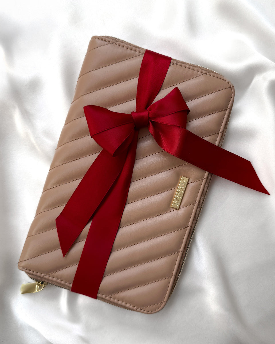 A product shot of the beige quilted Jewelry Travel Case from Syster P, tied with a large red satin bow.