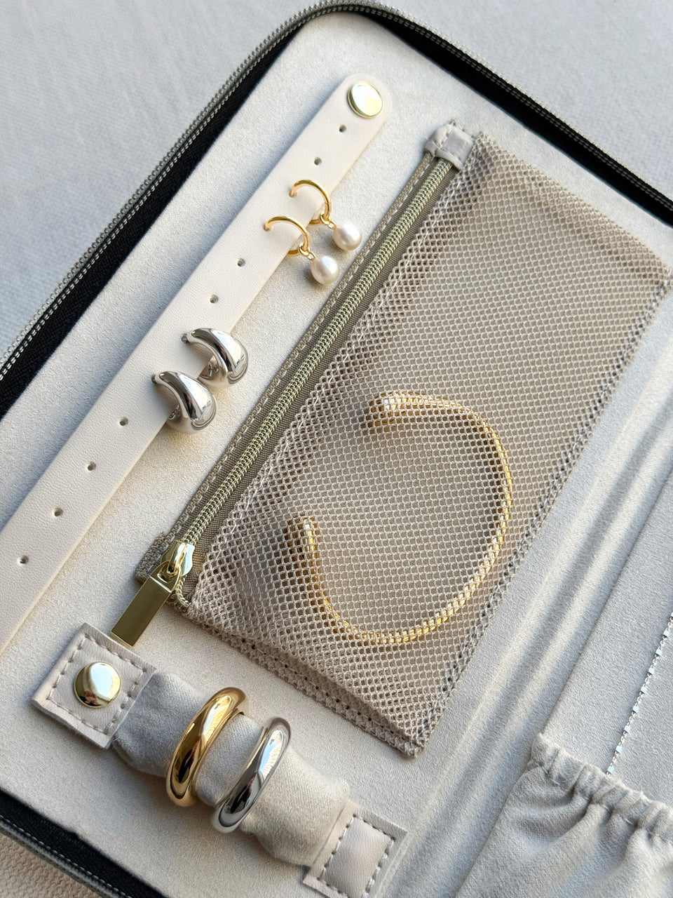 A close-up of the open Jewelry Travel Case in black, showing its beige interior neatly organizing gold and silver rings, pearl drop earrings, silver hoop earrings, and a gold bracelet.