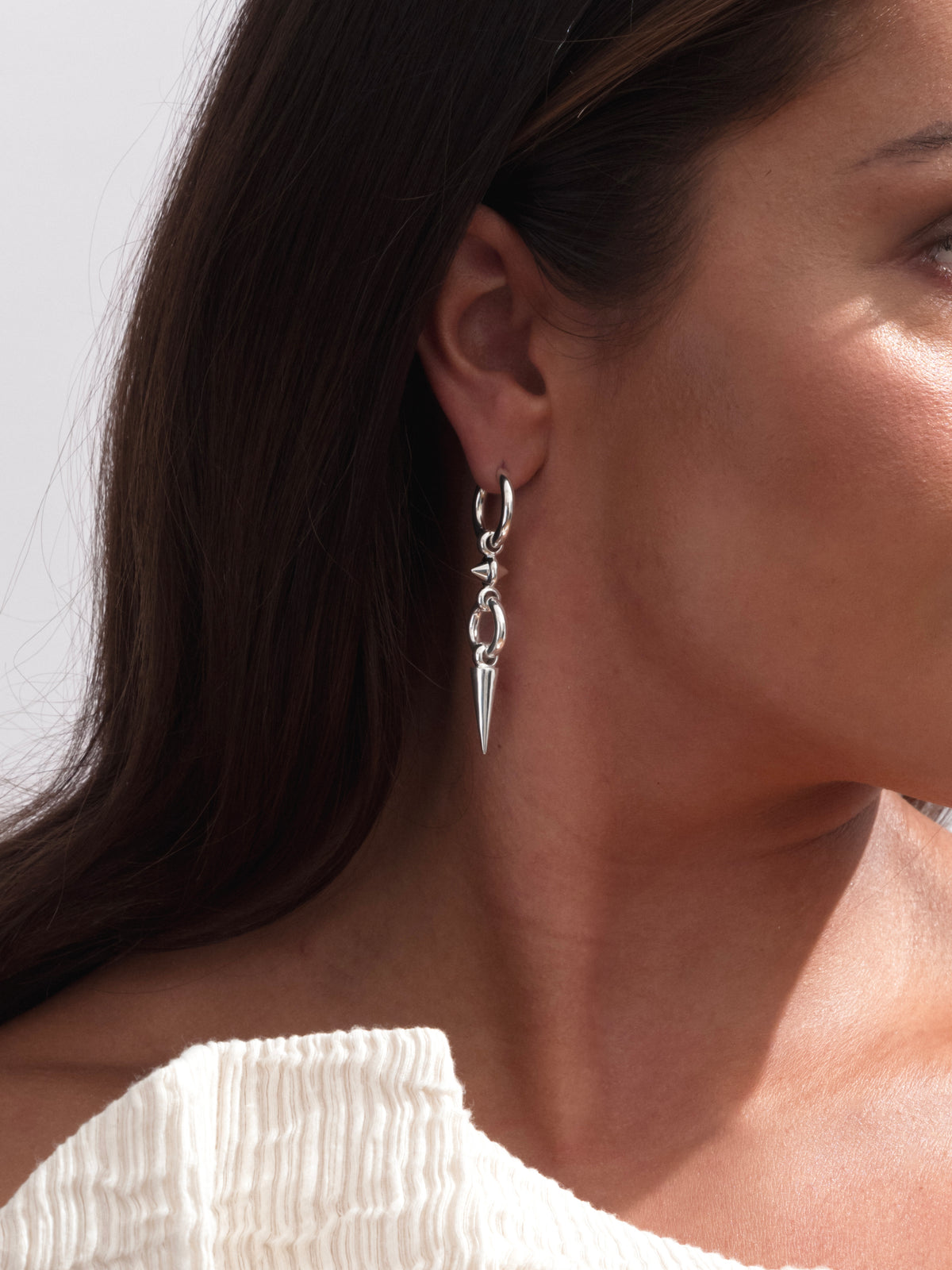 A close-up shot of a model wearing the Juno Long Single Earring in silver, which features a hoop with a long, dangling spike pendant.
