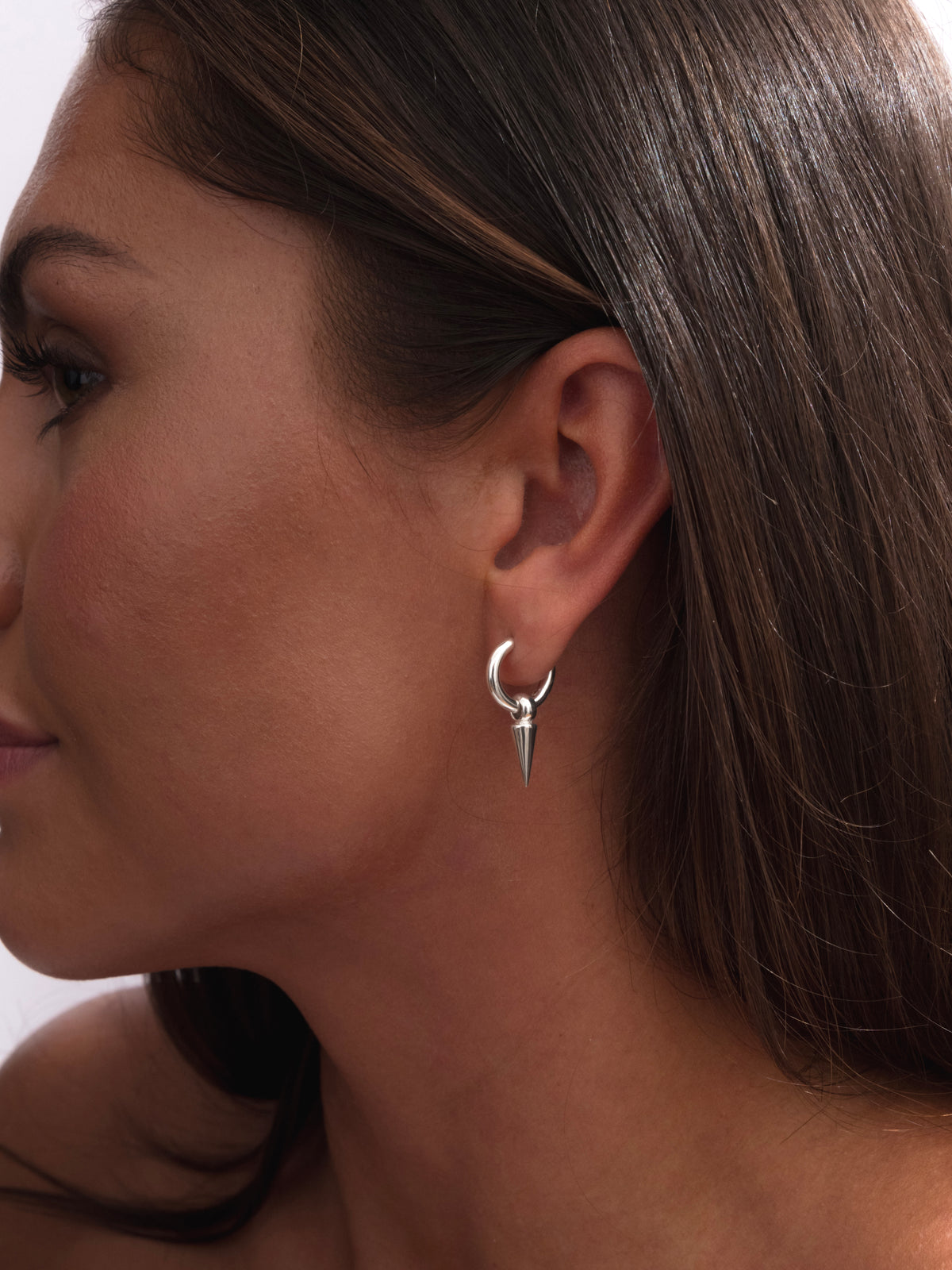 A close-up shot of a model wearing the Juno Hoop in silver, a small hoop earring with a dangling spike charm.