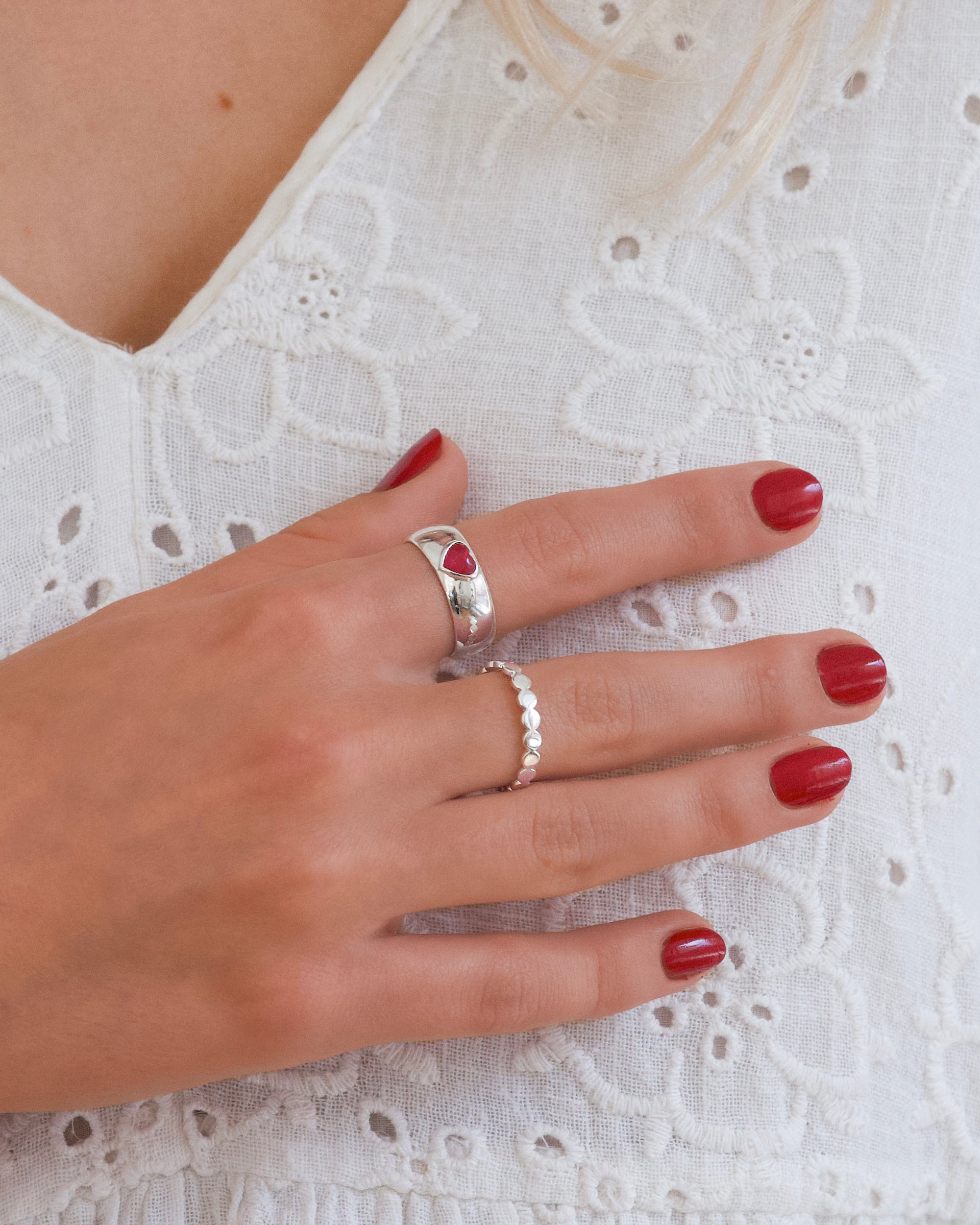 A model shot showcasing two Syster P rings: the delicate Beaches Flat Dots Ring in silver and the chunky LaLaLove Ring in silver, which features a small, inset red heart.