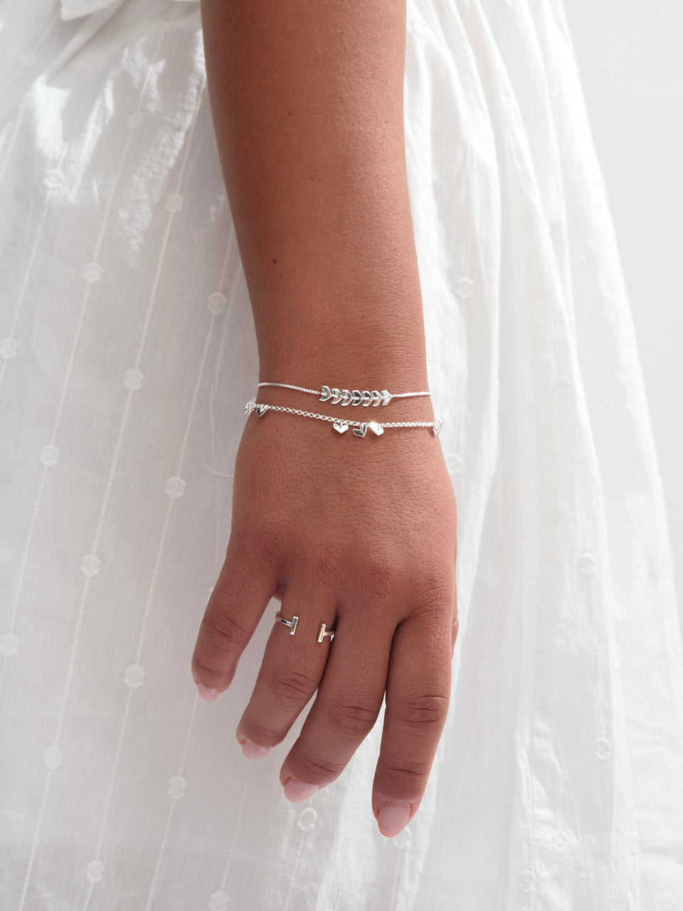 A model wears the open-ended Strict Bar Ring in silver, alongside two layered silver bracelets: the Layers Simone with its chevron design and the Layers Bianca with small heart charms.