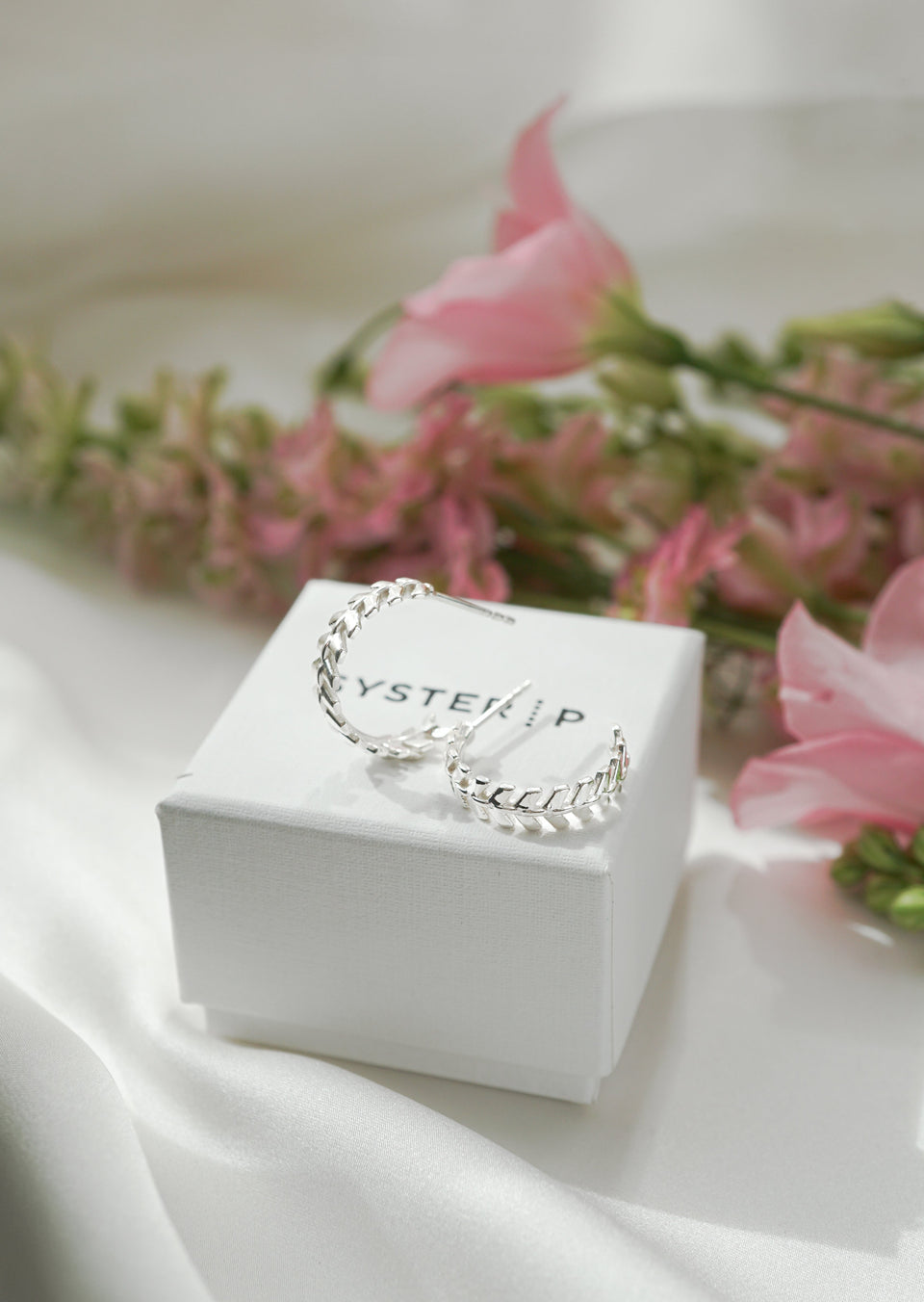 The Layers Olivia Hoops in silver resting on a white Syster P jewelry box, highlighting their beautiful leaf-like pattern.