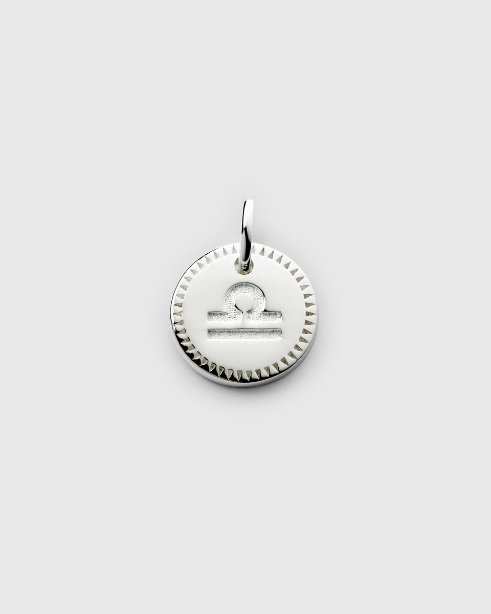 A product shot of the Beloved Zodie Pendant in silver, showing the engraved Libra zodiac symbol on a round charm with a decorative, textured border.