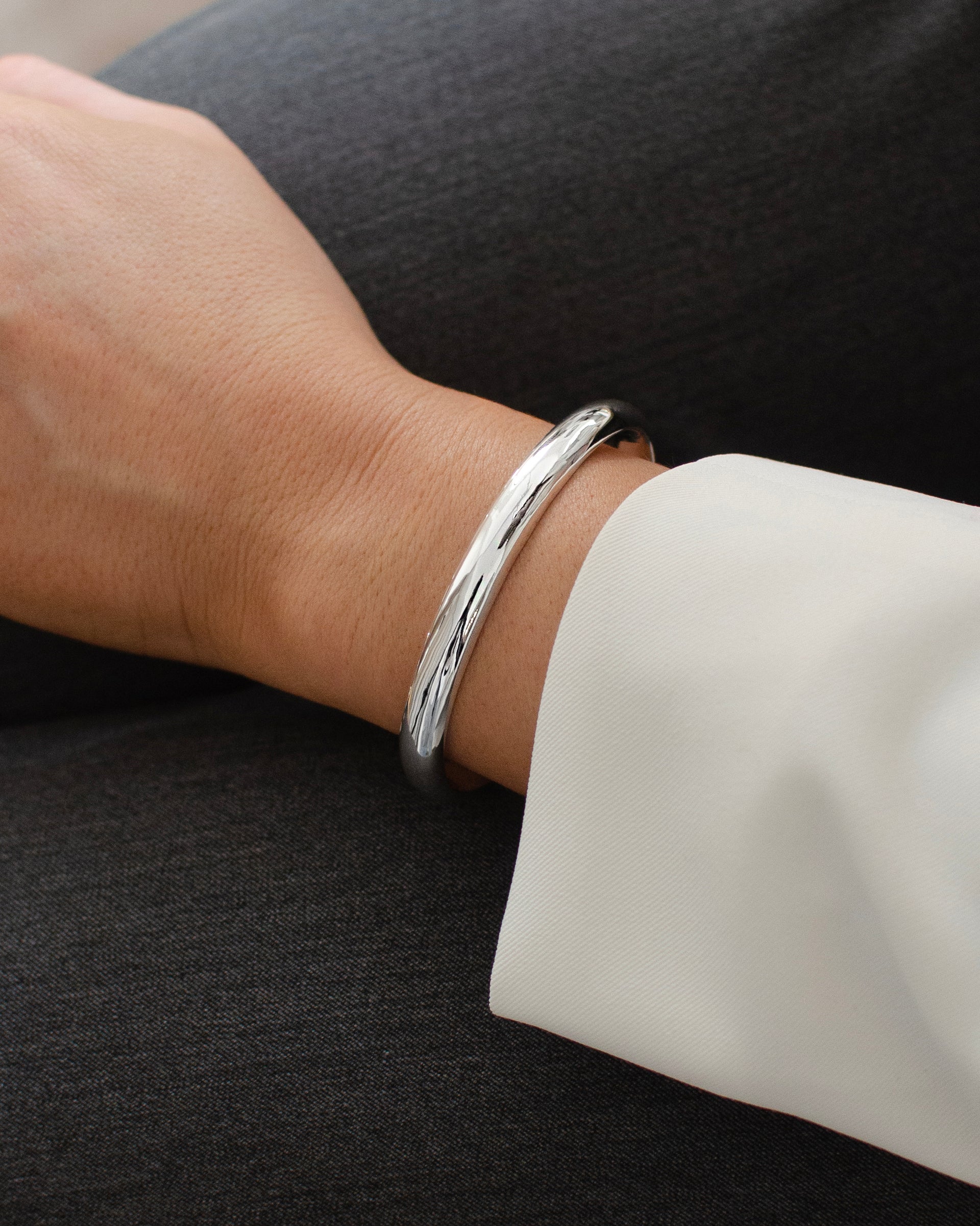 A close-up of a model's wrist wearing the Bolded Bangle in silver, showcasing its simple, chunky, and polished design.