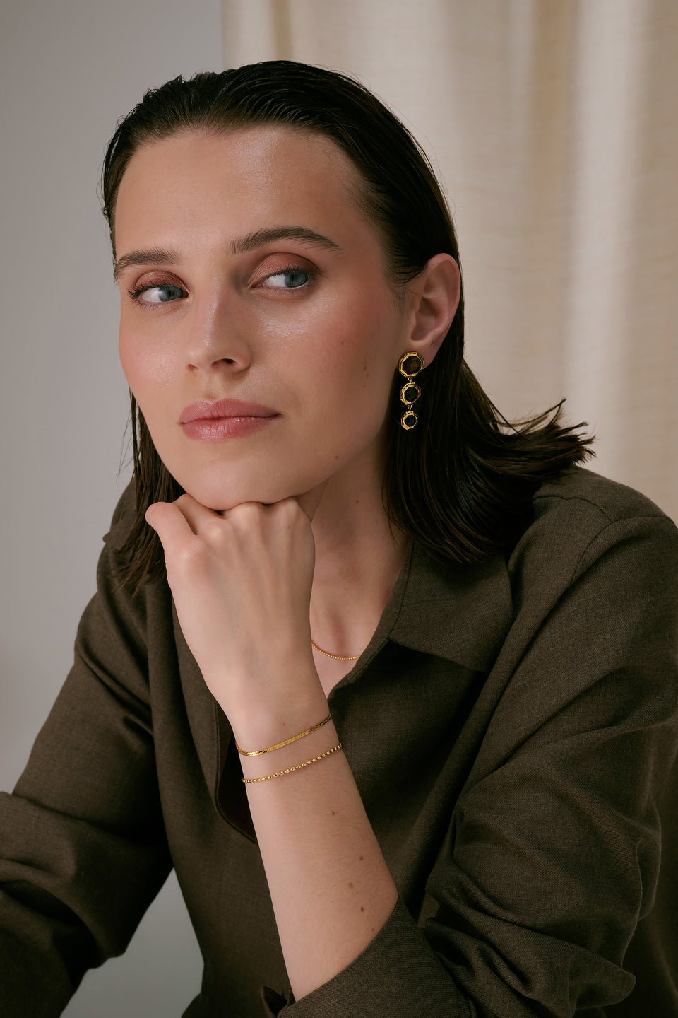 Long earrings featuring octagon-shaped smokey quartz stones and a two gold bracelets