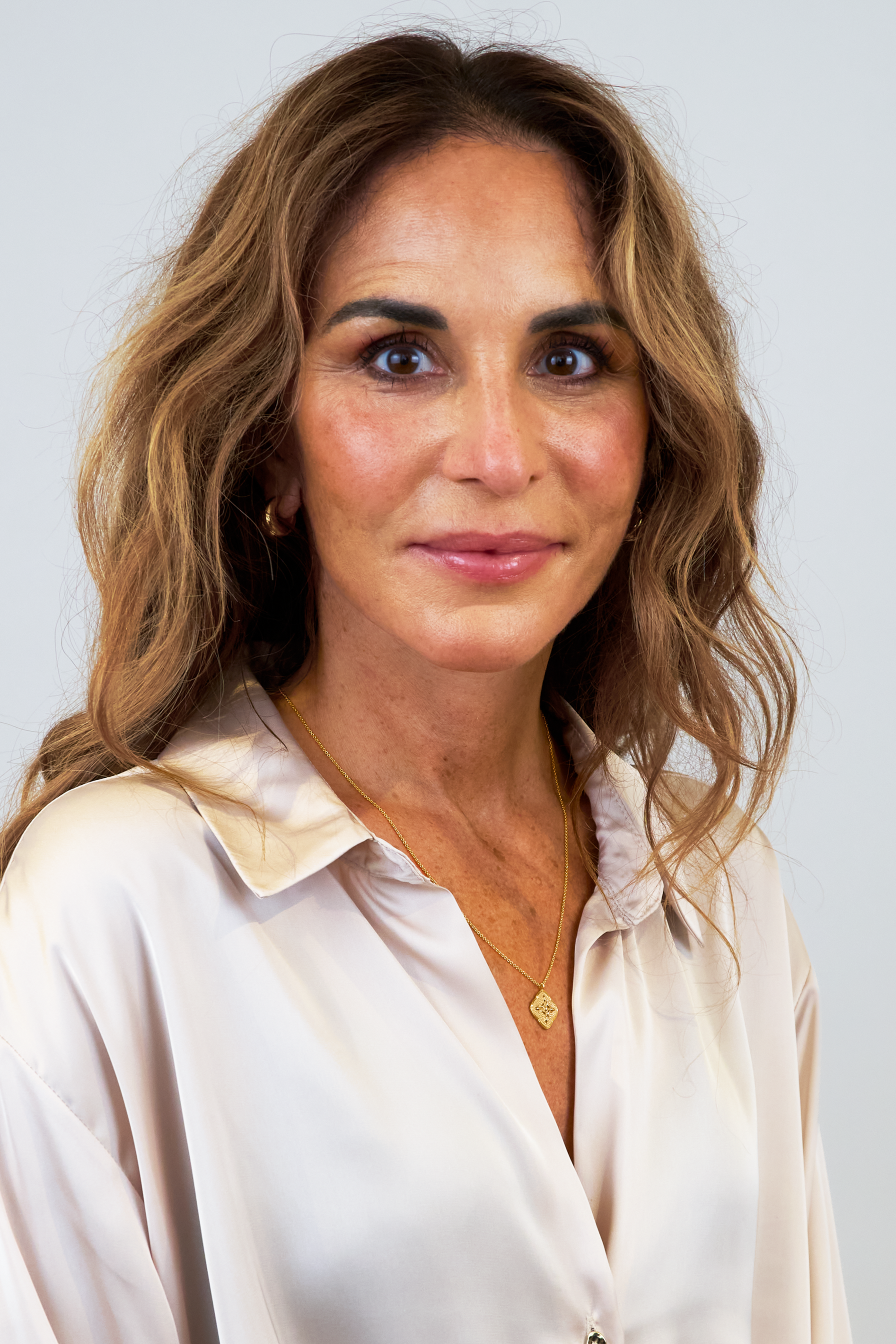 A portrait of a model wearing the Luna Necklace in gold, featuring a round, textured pendant, along with a pair of small gold hoop earrings.