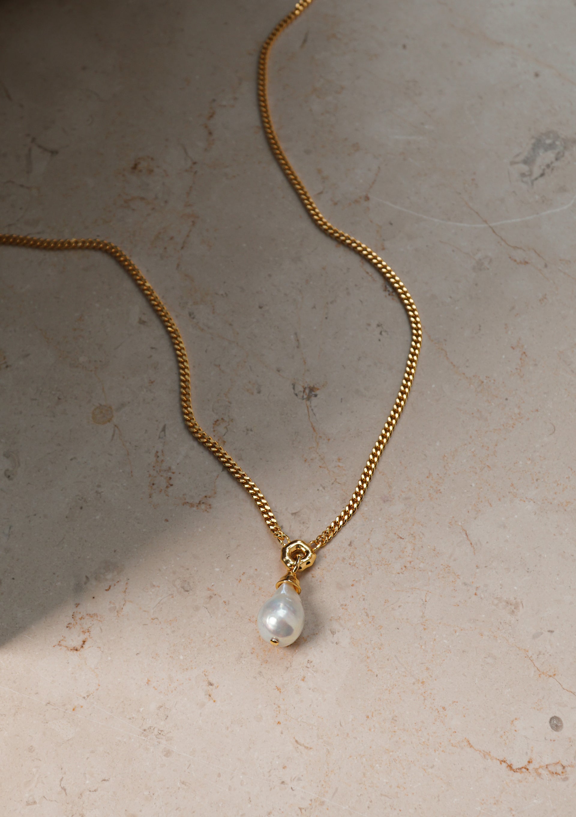 A product shot of the Mary Necklace in gold, laid out to display its heavy link chain and distinctive baroque pearl pendant.