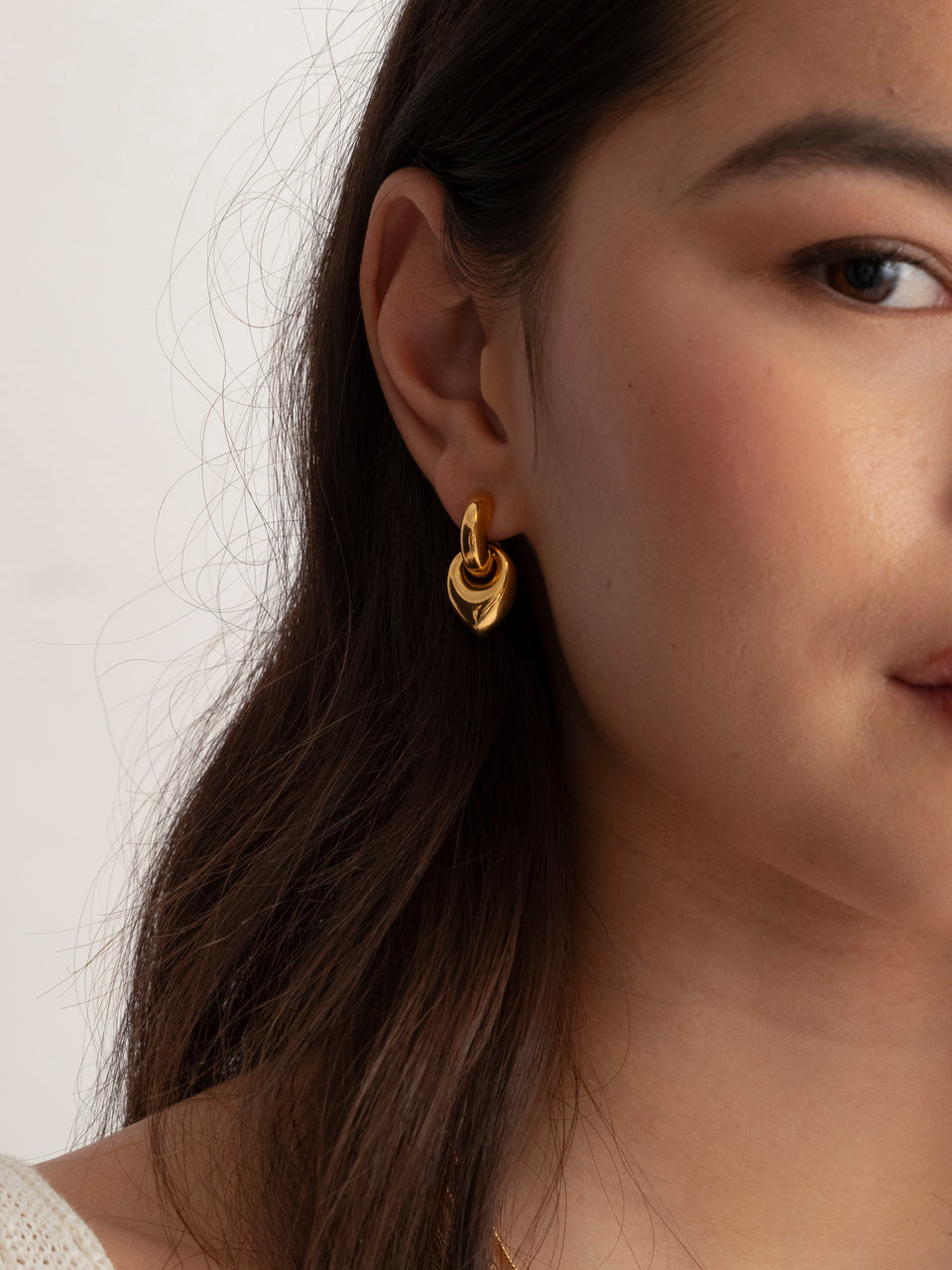 A close-up of a model wearing the Melinda Earrings in gold, featuring a chunky hoop and a leaf-shaped pendant, styled with the Florentina Necklace with green jade and the Santa Monica Necklace with green onyx.