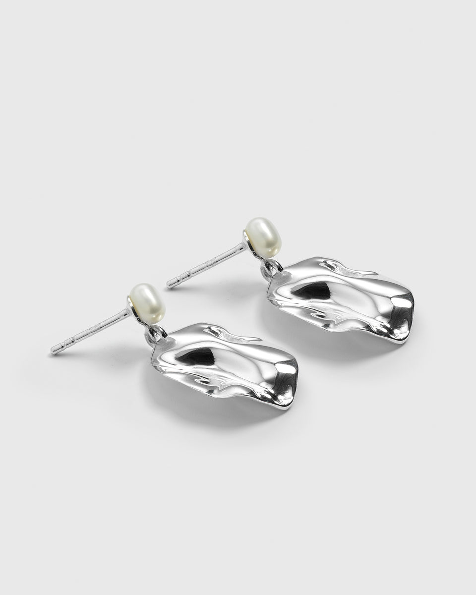 A product shot of the Moulded Short Earrings in silver, featuring an organic, irregularly shaped dangling pendant and a freshwater pearl stud.