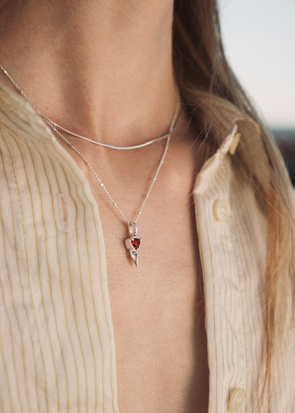 A close-up of a model wearing the Mrs H Spike Necklace in silver, featuring a pendant with a spike and a red garnet, layered with a second, simple silver snake chain.