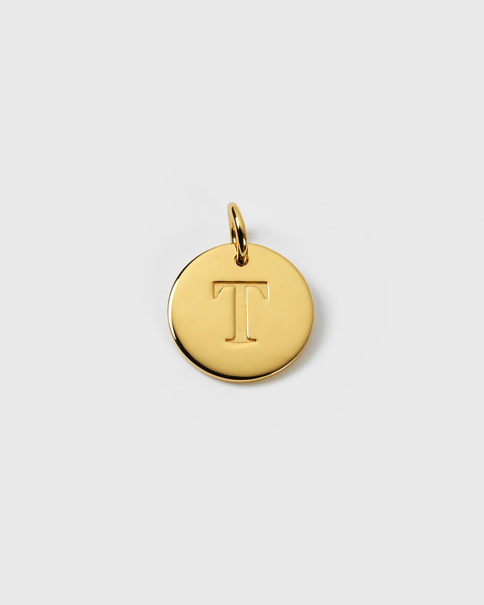 A product shot of the gold Beloved Big Letter charm, a round pendant featuring the engraved letter 'T'.