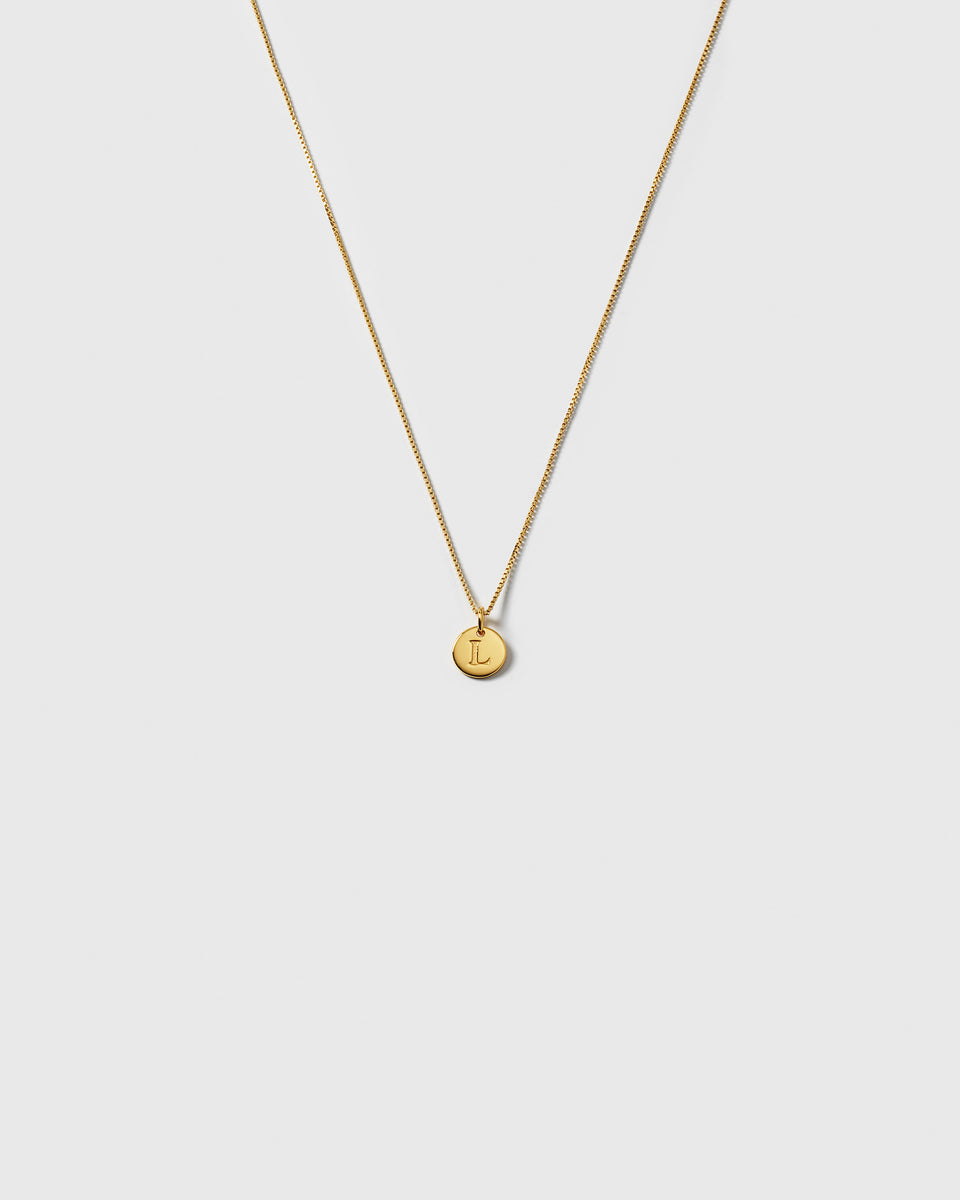 A product shot of the Beloved Short Box Chain in gold, styled with a small, round pendant engraved with the letter L.