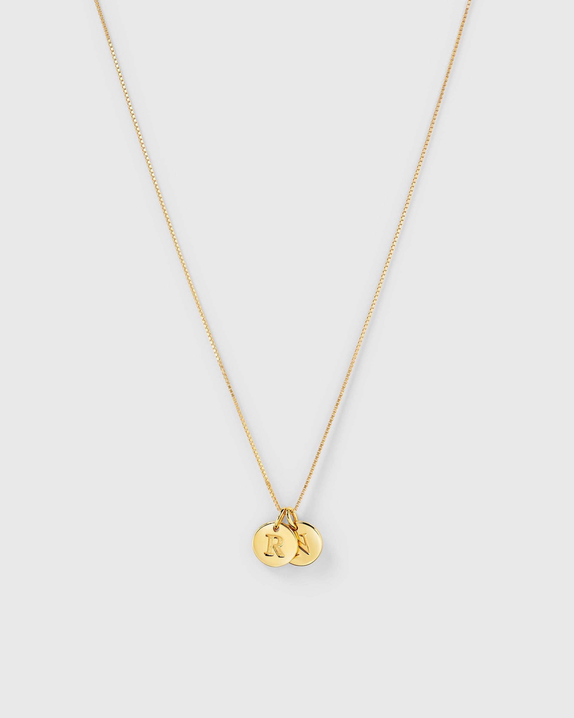 A product shot of the Beloved Medium Box Chain in gold, styled with two Beloved Mini Letter charms featuring the initials 'R' and 'N'.