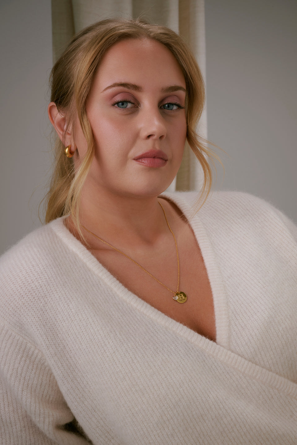 A close-up shot of a model wearing the Beloved Medium Rolo Chain in gold, styled with a round gold pendant featuring the letter H and an crystal heart charm