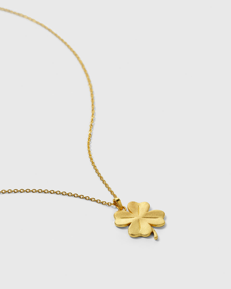 A close-up image of the gold Beaches Fortune Necklace, detailing its matte-textured four-leaf clover pendant and the delicate oval link chain.