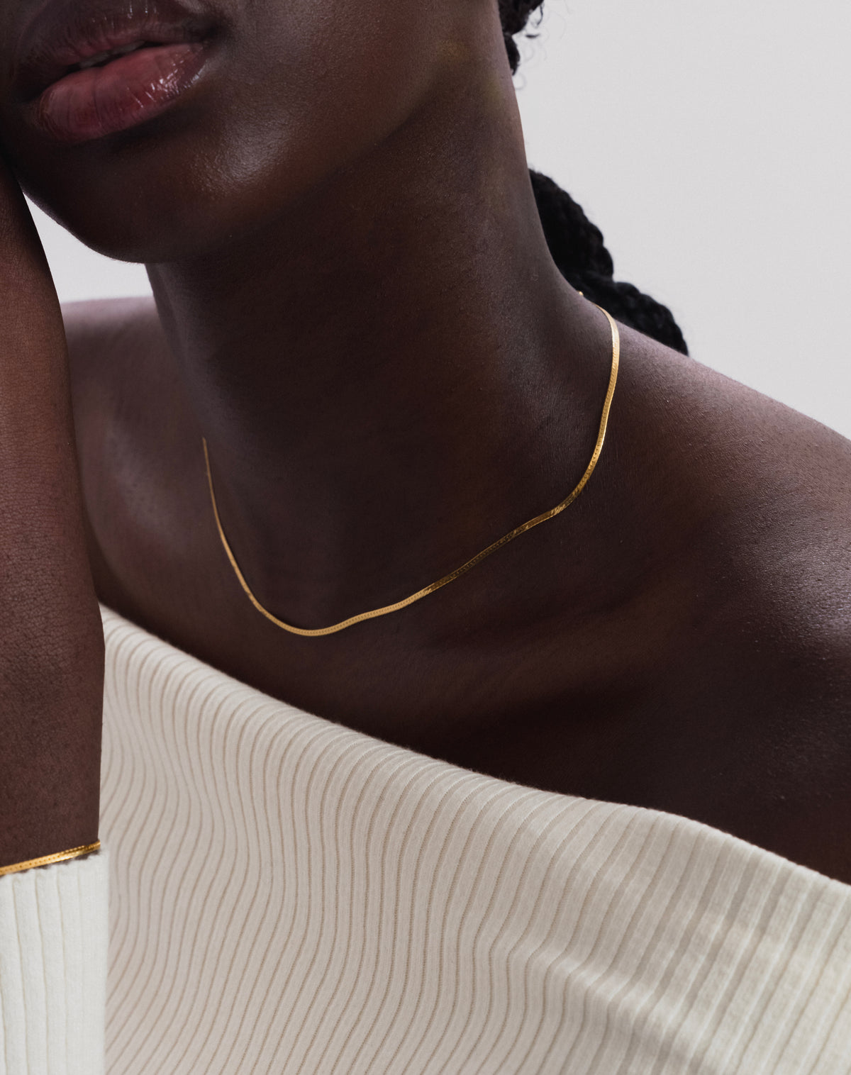 A close-up of a model wearing the Herringbone Necklace in gold, a delicate flat chain, along with a matching herringbone bracelet on her wrist.