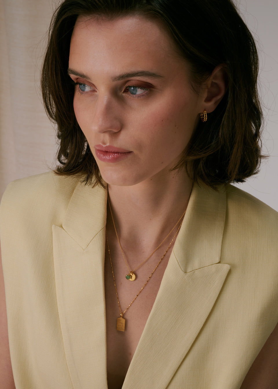 A necklace, layered with a longer gold chain necklace and paired with small gold hoop earrings.