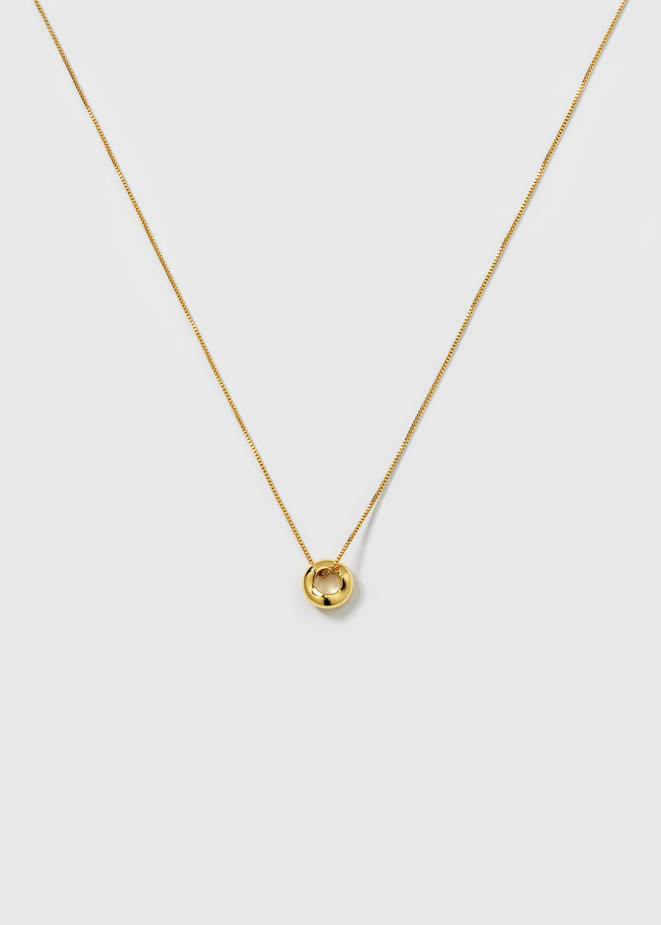 A product shot of the Bolded Wavy Necklace in gold, featuring a smooth chain and a shiny, circular pendant with a wavy design.