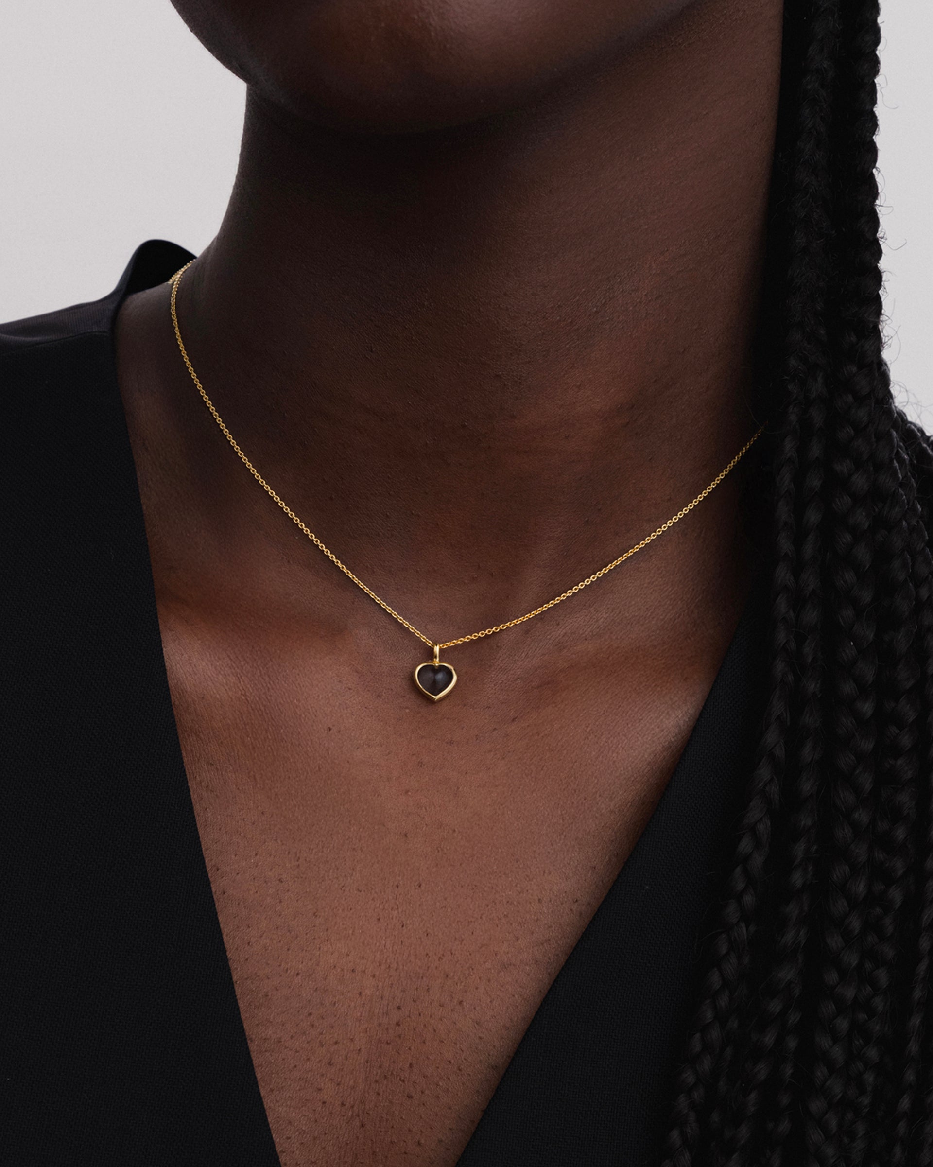 Close-up of a model wearing the La La Love Necklace in gold, featuring a delicate chain and a heart-shaped smokey quartz pendant.