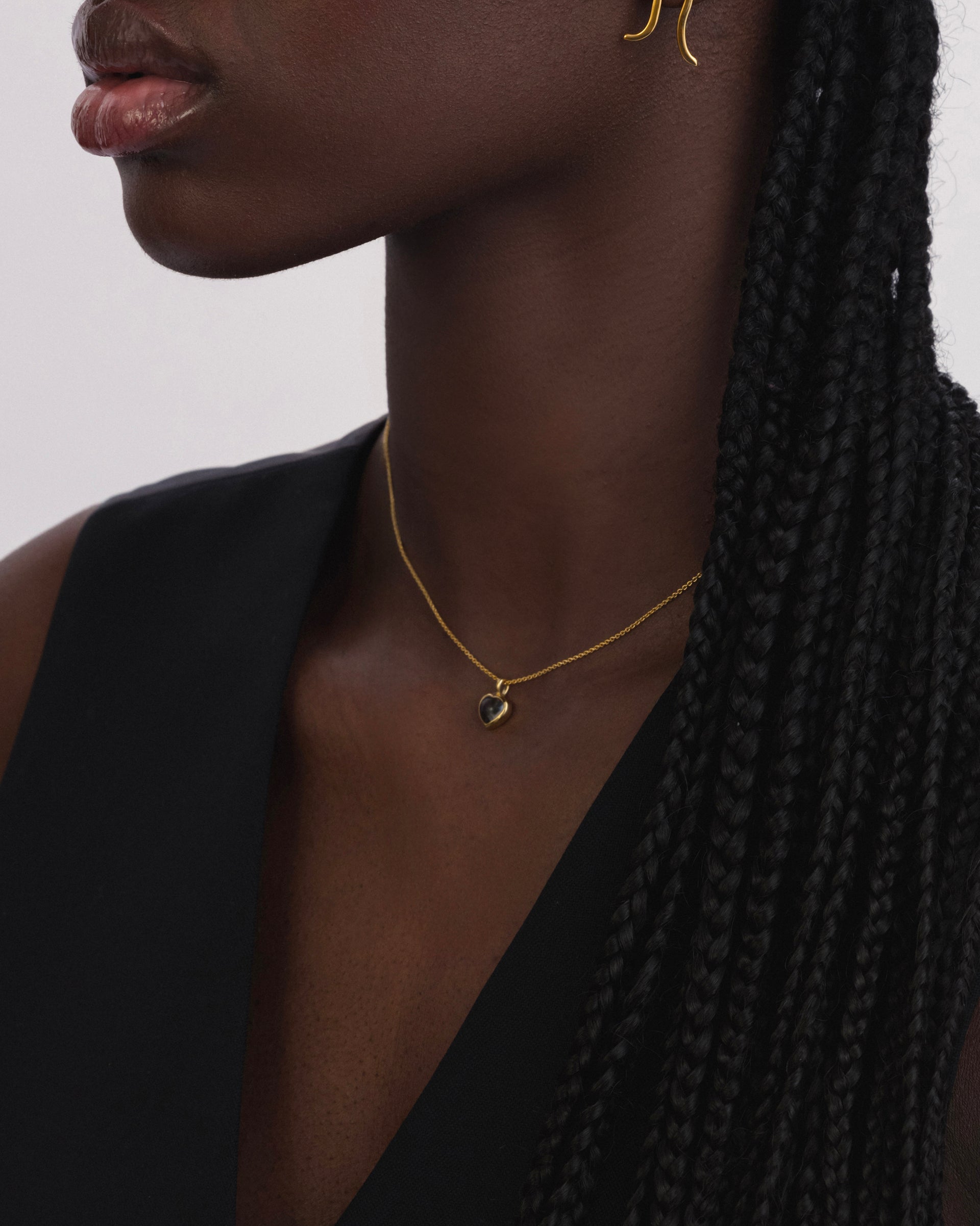 A model wearing the La La Love Necklace in gold with a smokey quartz heart pendant, styled with a gold earring.