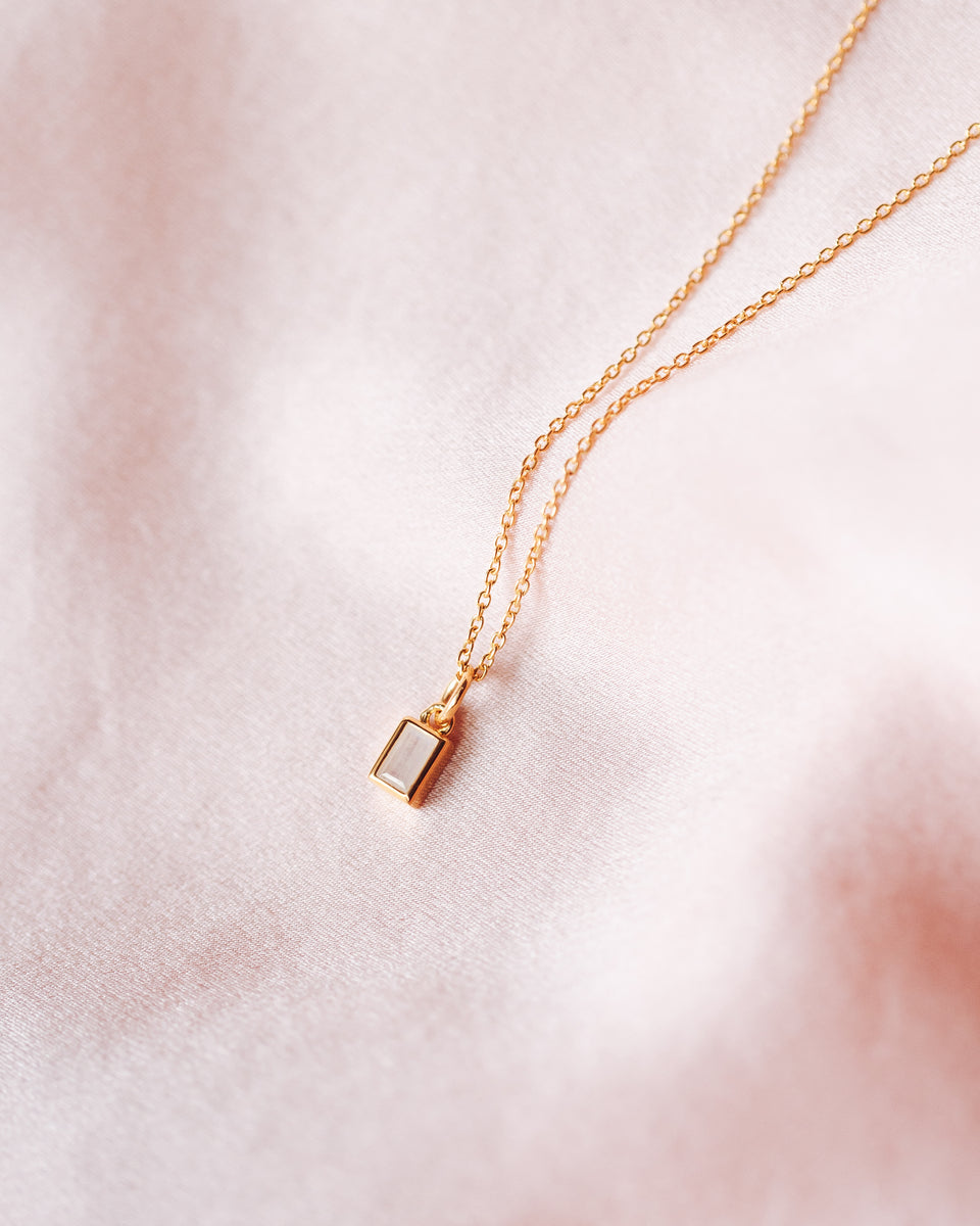 A product shot of the Beloved Squared Pendant Gold, showing the small rectangular pendant with a moonstone on a fine gold chain.