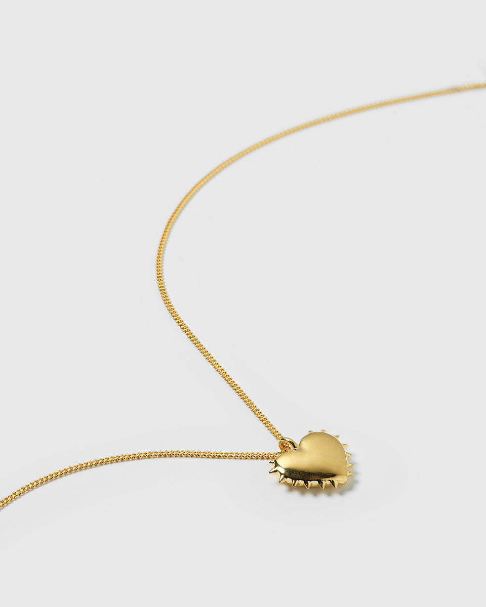 A close-up product shot of the True Love Spike Heart Necklace in gold, showing the detailed heart pendant with its spiky edge and the fine chain.