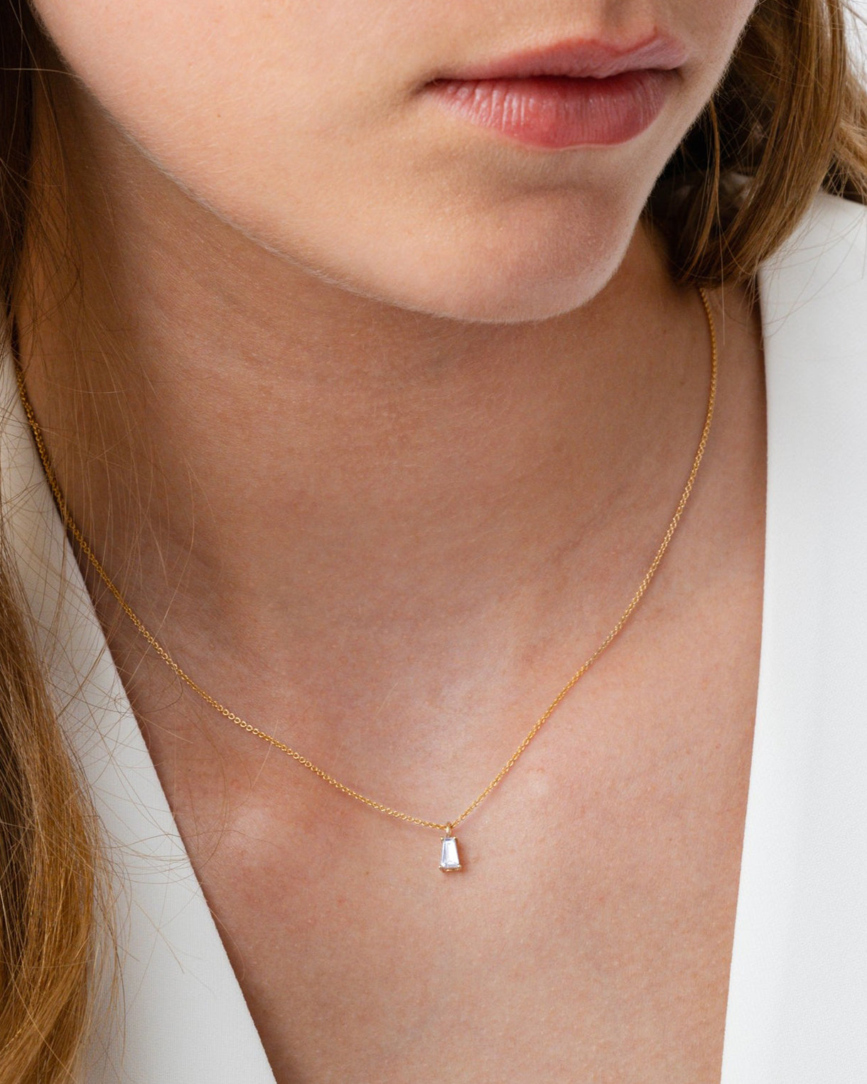 A close-up of a model wearing the Iggy Necklace in gold, featuring a delicate chain and a single tapered baguette-cut cubic zirconia pendant.