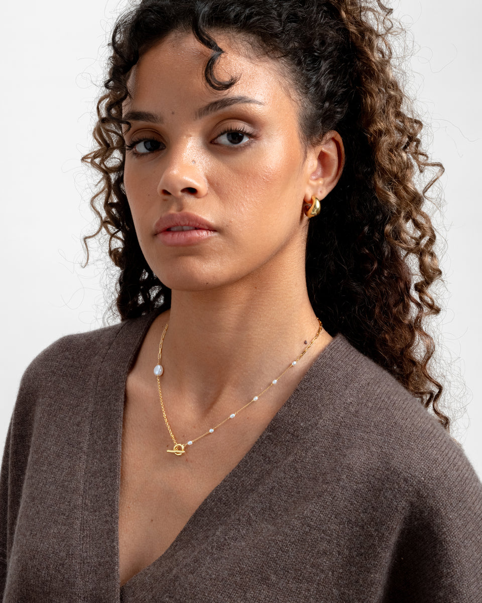 Model wearing the Paxton Short Necklace Gold, showcasing its mixed gold links, baroque pearls, and front toggle clasp.