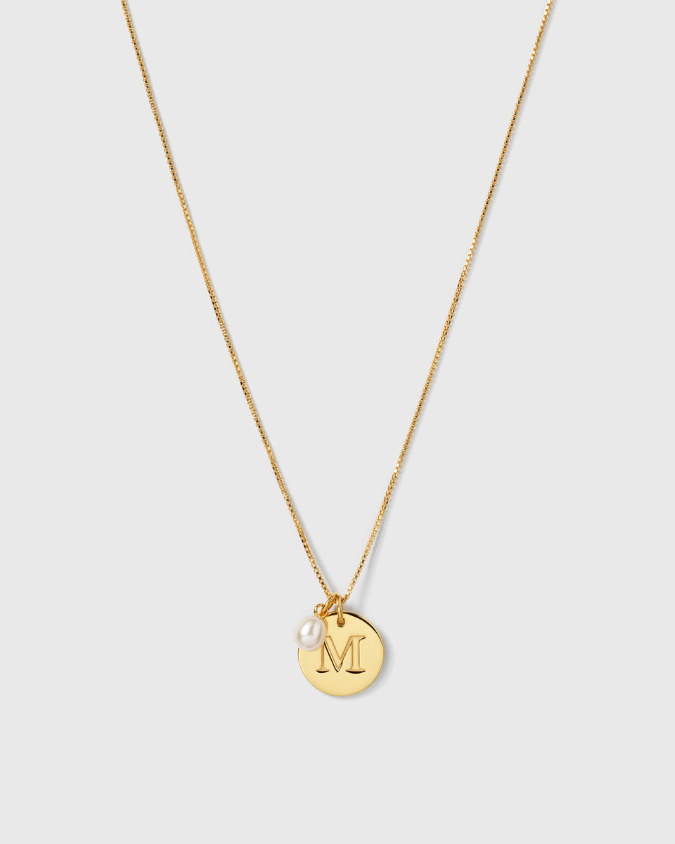 A gold necklace with a fine box chain, featuring the Beloved Pearl Pendant and a circular gold pendant engraved with the letter 'M'.