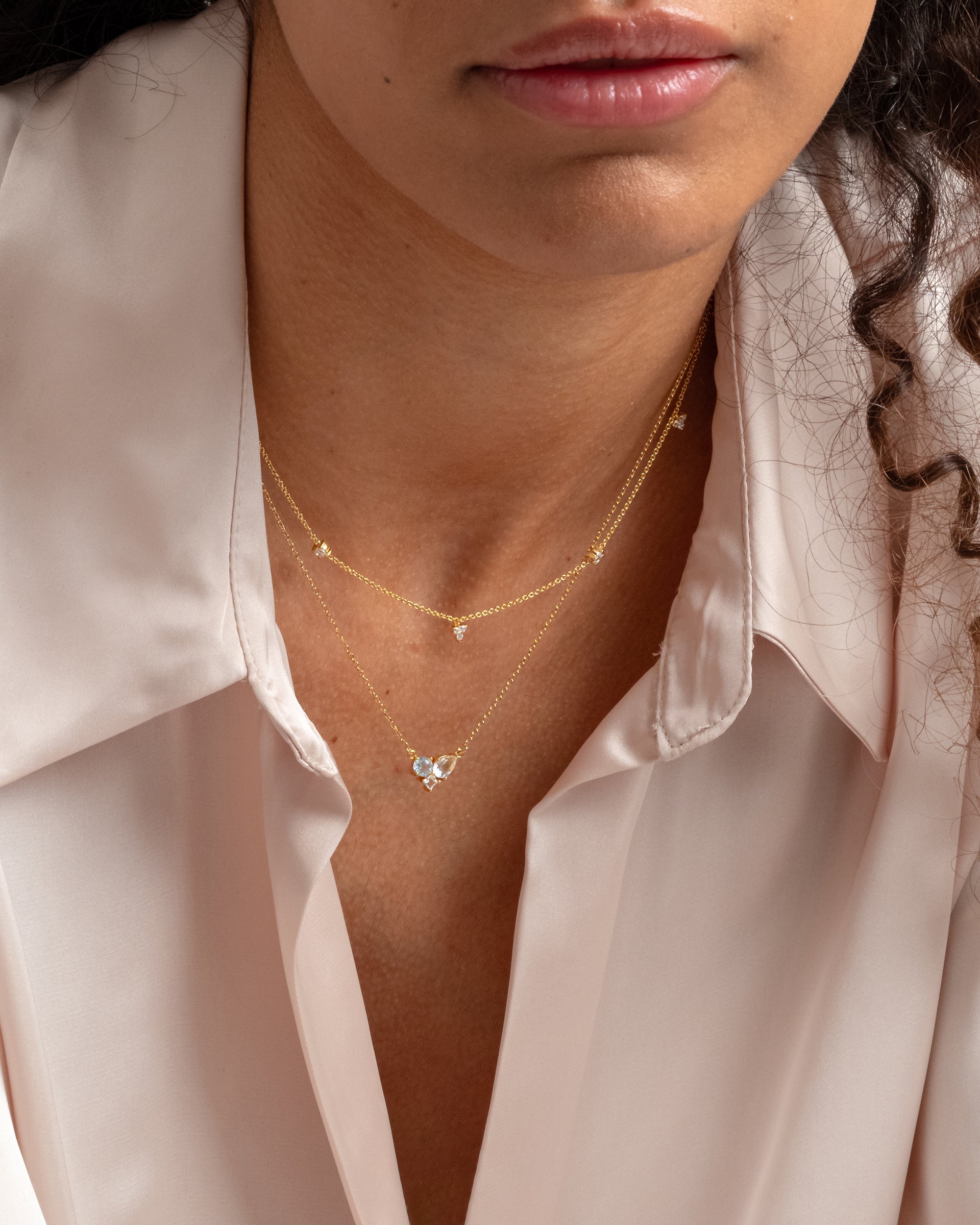 A close-up of a model wearing the Celestia Necklace in gold, featuring a delicate chain with sparkling, varied cubic zirconia stones, layered with another gold necklace.