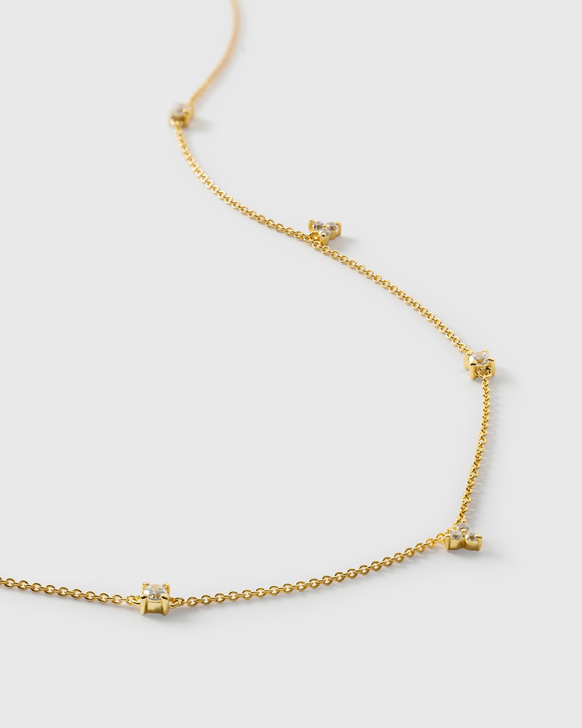 A product shot of the Celestia Necklace in gold, with a close-up view of its delicate chain adorned with sparkling, variously shaped cubic zirconia stones.
