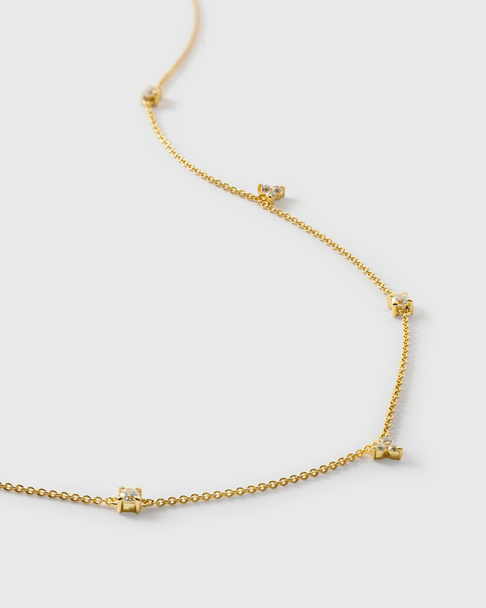 A product shot of the Celestia Necklace in gold, with a close-up view of its delicate chain adorned with sparkling, variously shaped cubic zirconia stones.