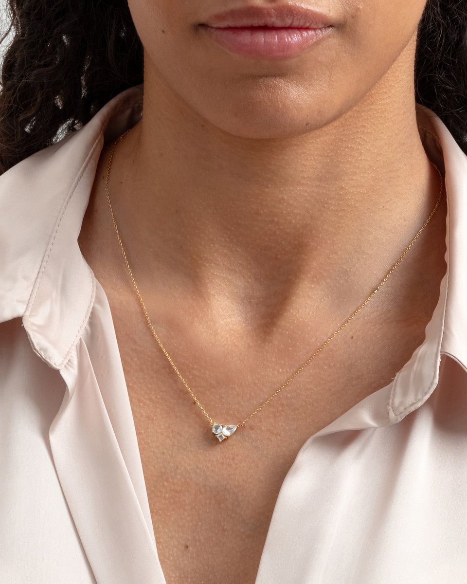 A close-up shot of a model wearing the Pam Necklace in gold, featuring a pendant with a beautiful cluster of white topazes.