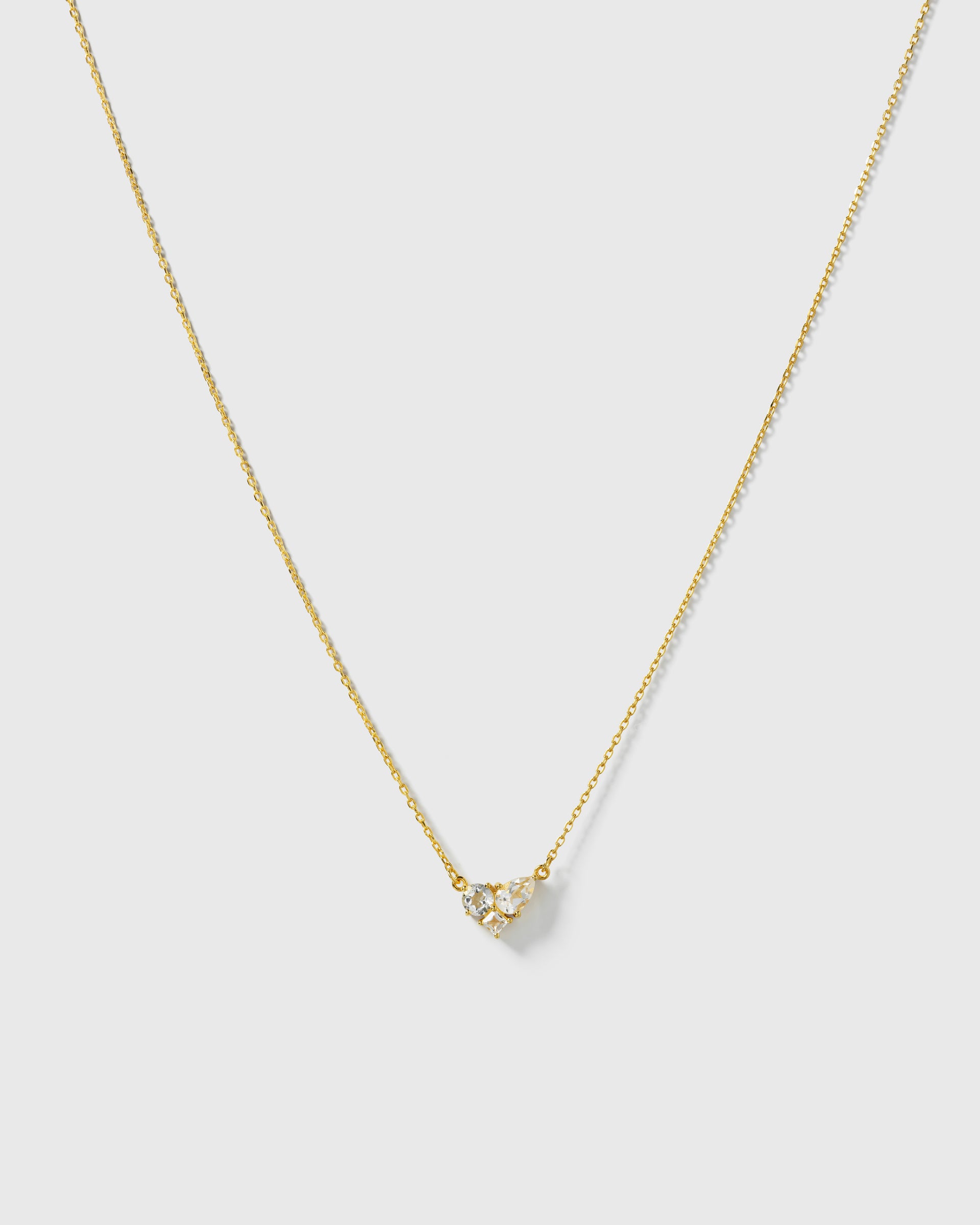 A product shot of the Pam Necklace in gold, displaying its fine chain and a sparkling pendant made of clustered white topazes in different cuts.