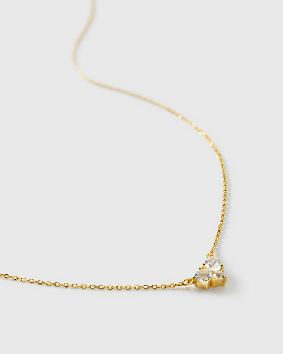 A close-up product shot of the Pam Necklace in gold, displaying its delicate chain and the sparkling pendant with a cluster of white topazes in various shapes.