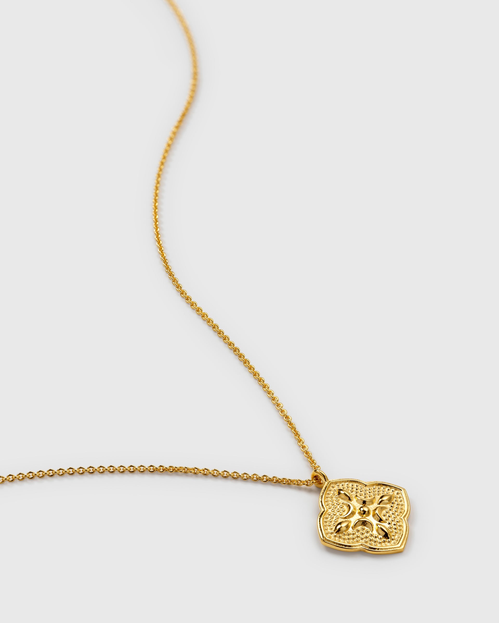 A close-up product shot of the Luna Necklace in gold, showcasing the intricate moon-inspired pattern on its square pendant and the delicate oval chain.