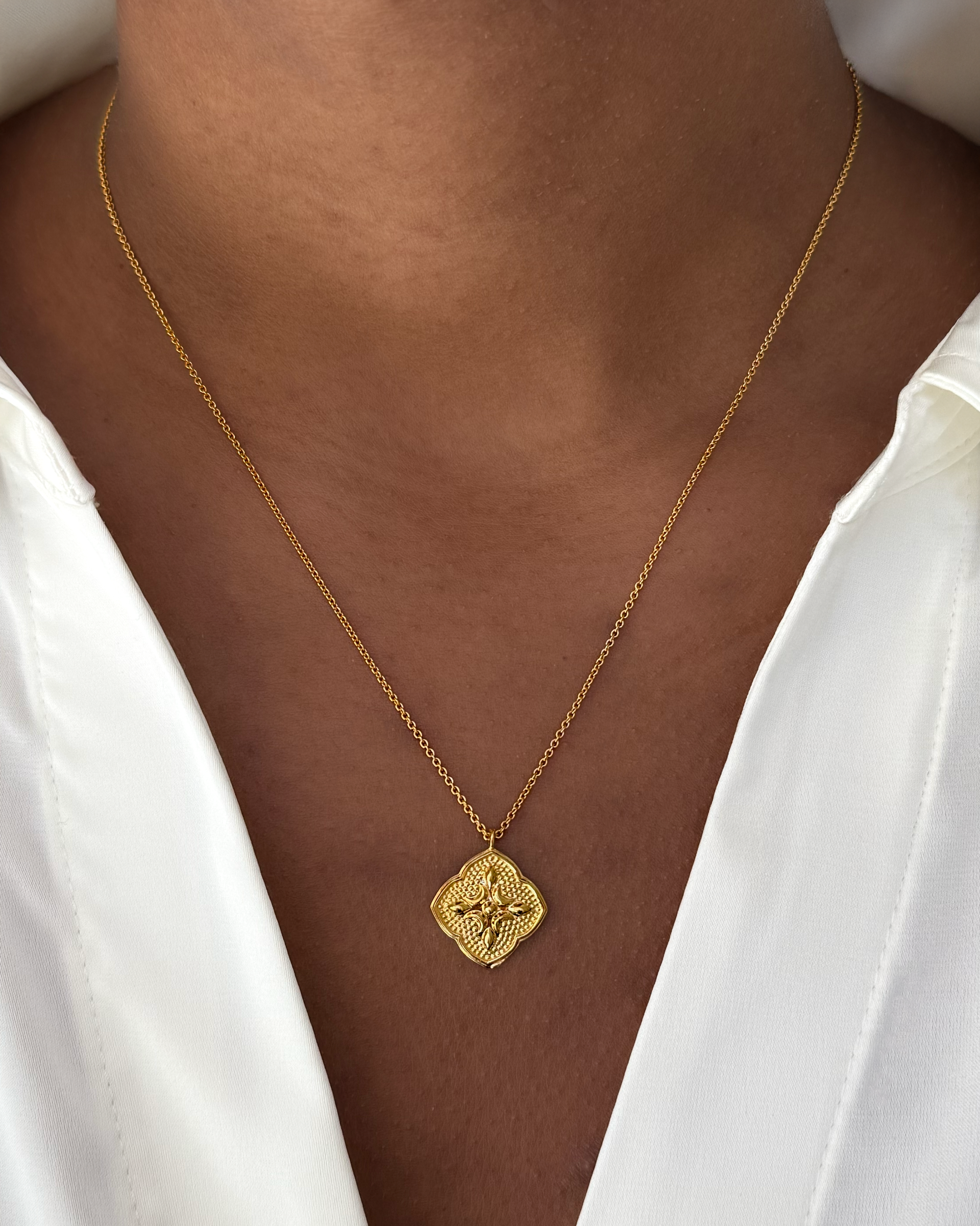 A close-up shot of a model wearing the gold Luna Necklace, which features a delicate chain and an ornate, quatrefoil-shaped pendant.
