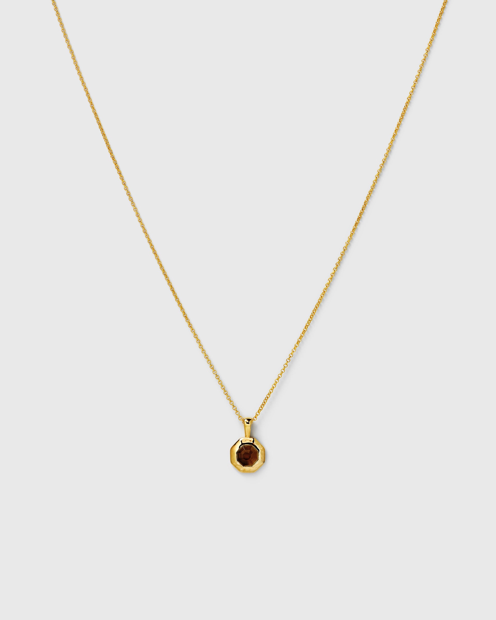 A necklace in gold, featuring a fine chain and an octagonal pendant set with a faceted smokey quartz stone.