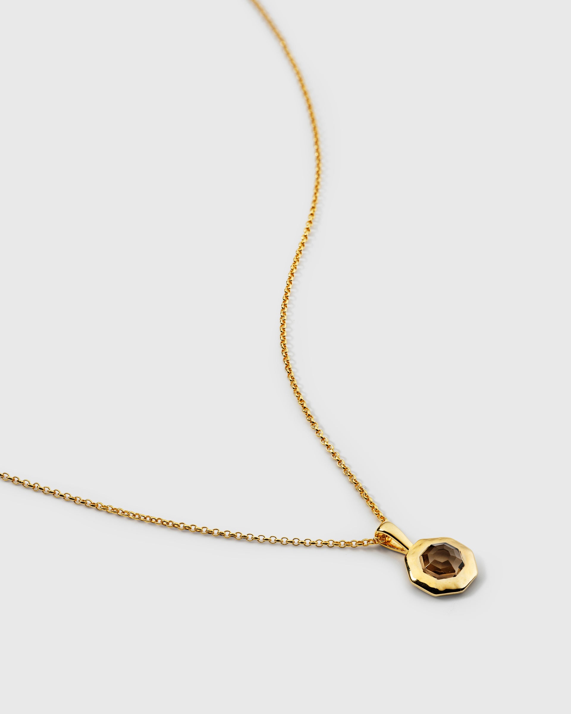 A necklace in gold, featuring a delicate chain and an octagonal pendant set with a faceted smokey quartz stone.