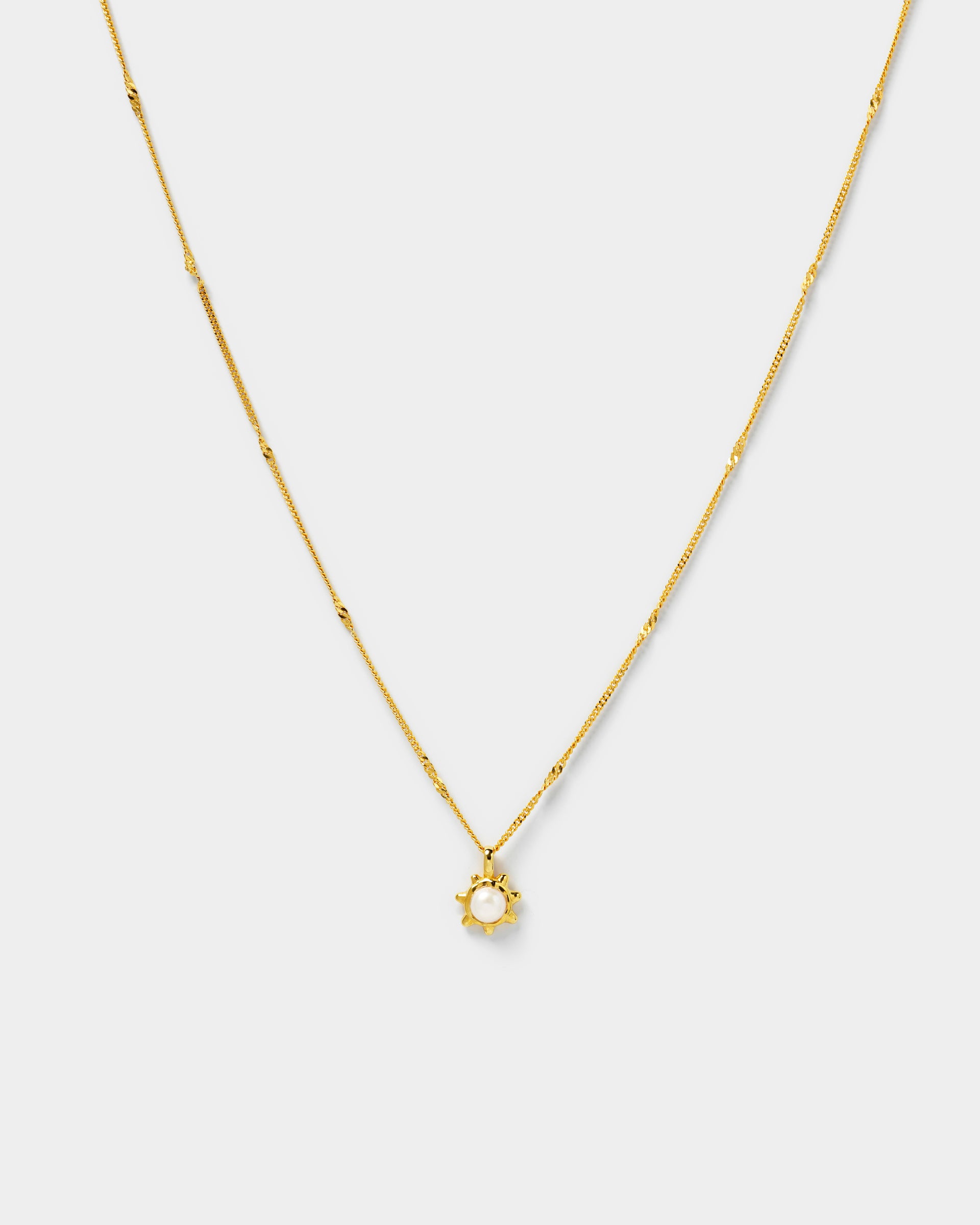 A gold necklace with a delicate chain and a sun-shaped pendant holding a single freshwater pearl.