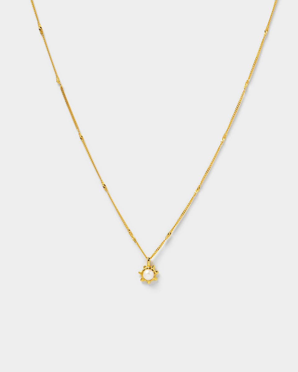 A gold necklace with a delicate chain and a sun-shaped pendant holding a single freshwater pearl.
