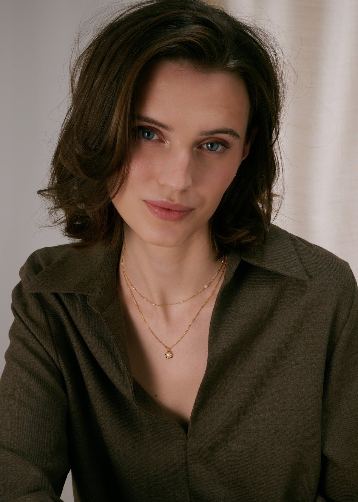 Gold layered necklaces, one with a sunburst pendant featuring a pearl, and a shorter chain decorated with freshwater pearls.