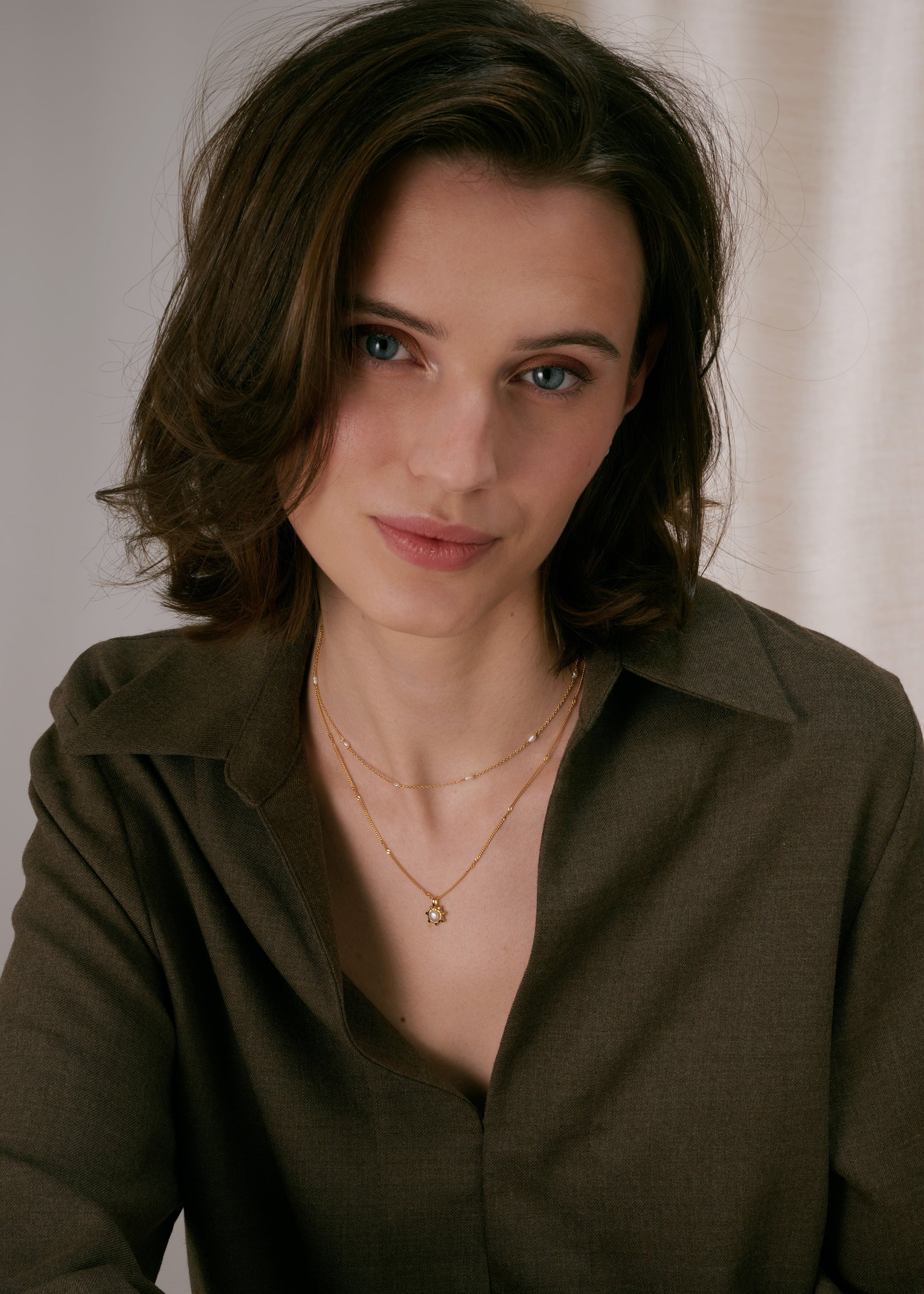 Gold layered necklaces, one with a sunburst pendant featuring a pearl, and a shorter chain decorated with freshwater pearls.