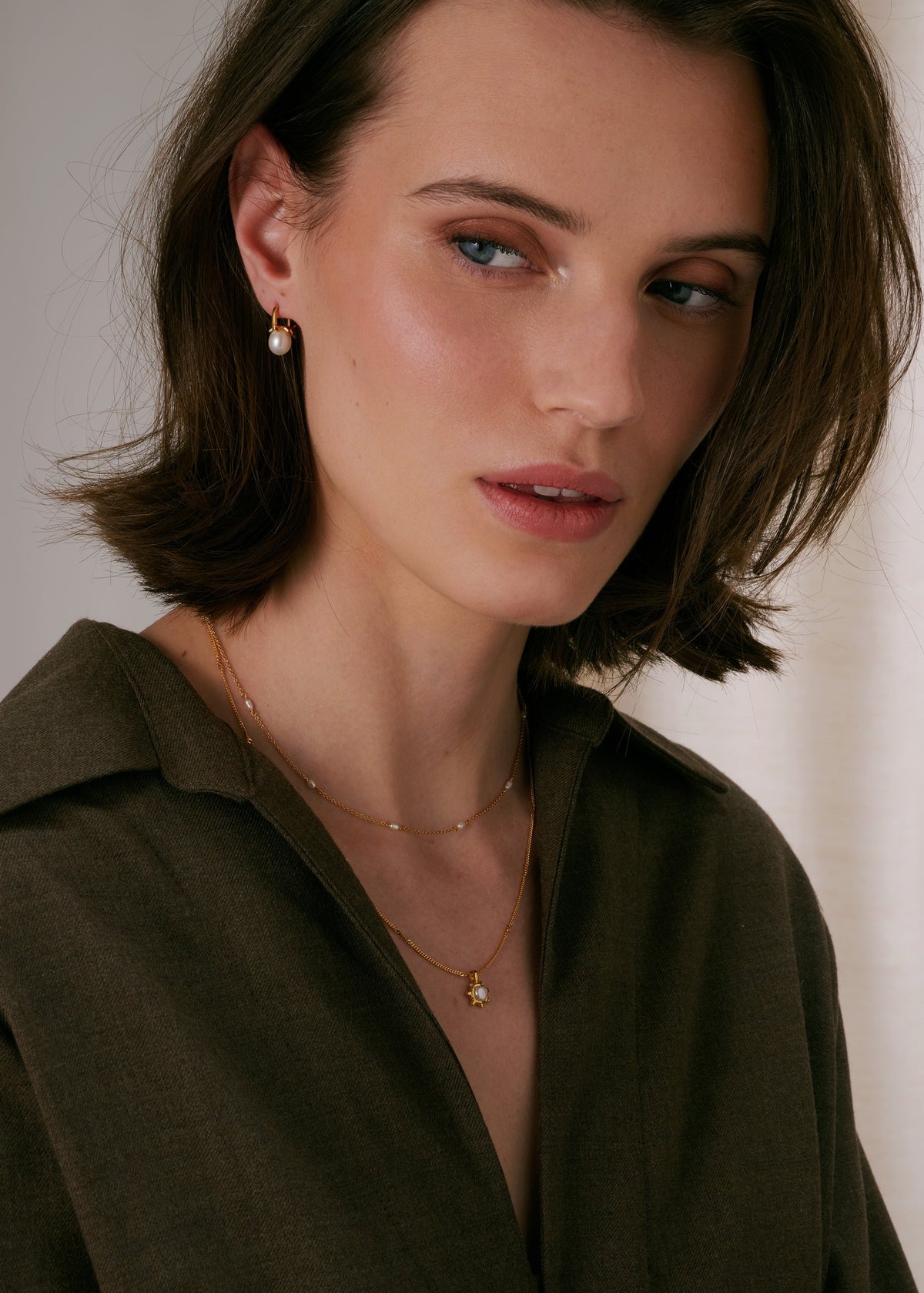 Necklace in gold, layered with a second delicate pearl chain, and matching gold and pearl earrings.
