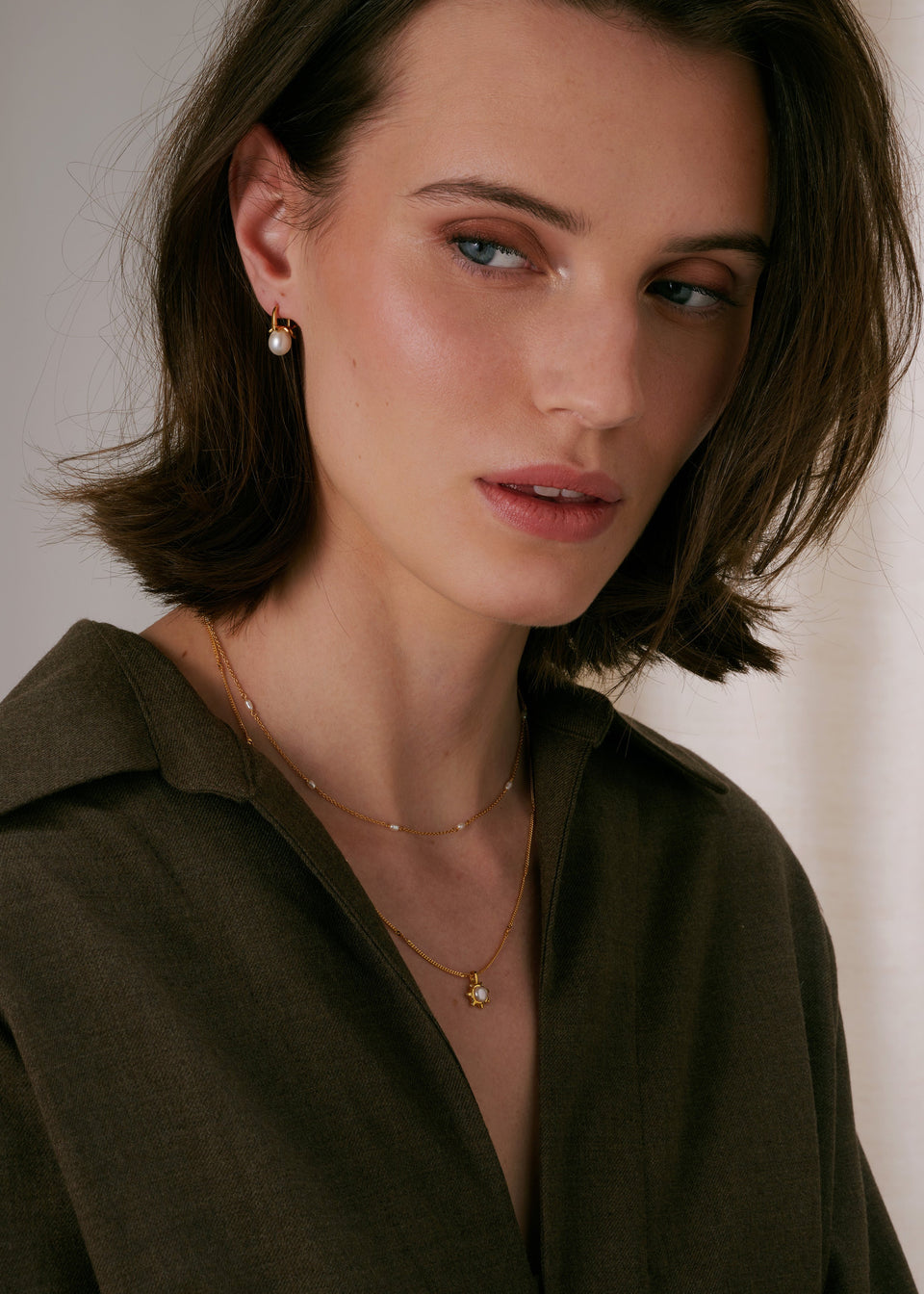 Necklace in gold, layered with a second delicate pearl chain, and matching gold and pearl earrings.